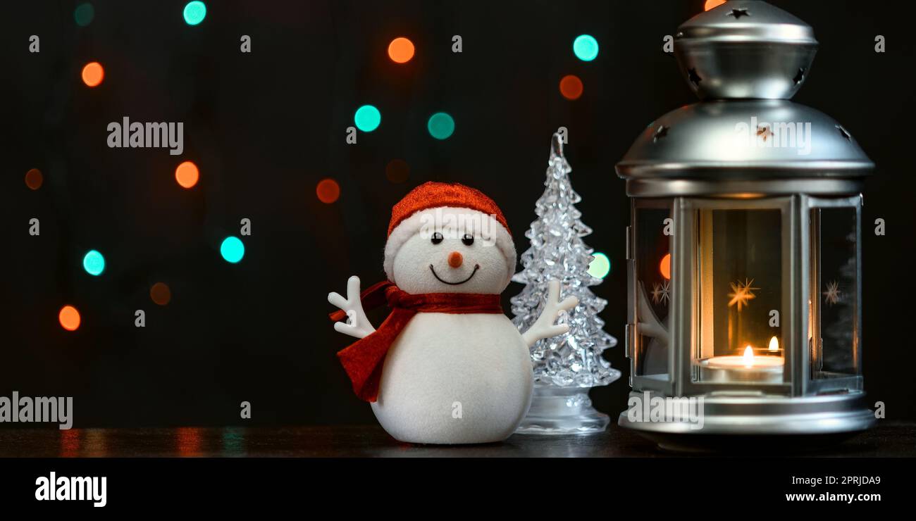 Christmas card: a snowman, a lantern with candles and blurry lights in the background. Stock Photo
