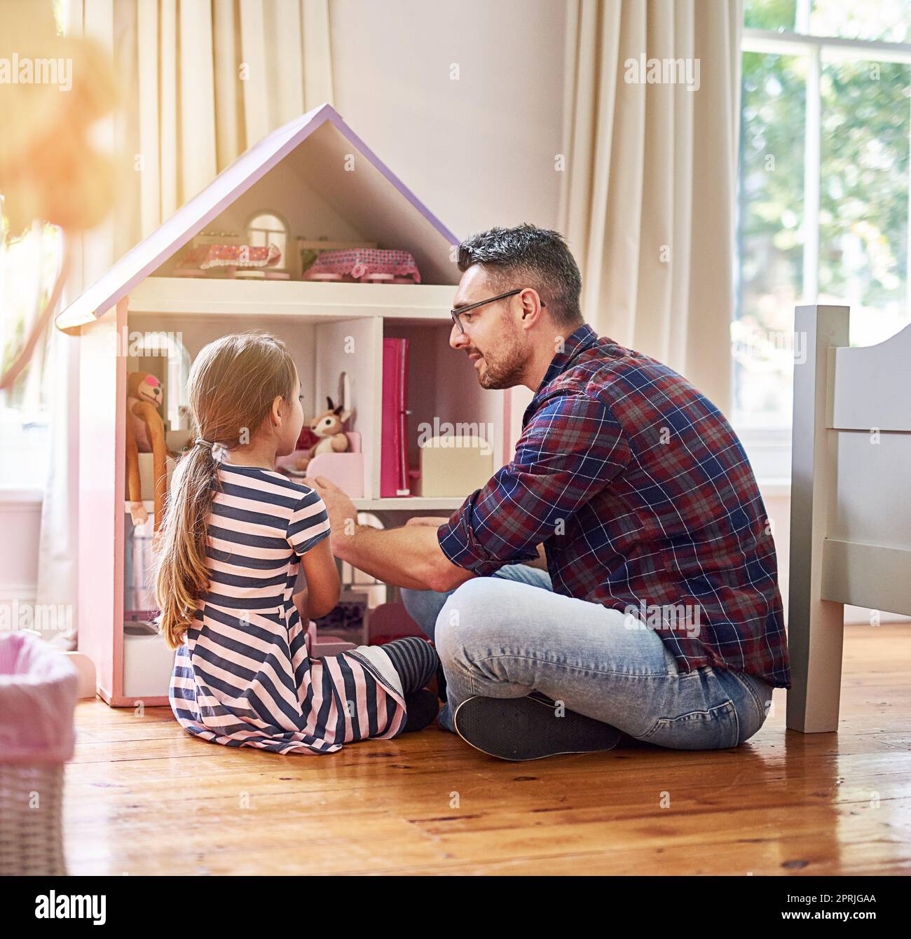 Giving her daddy the grand tour. Rearview shot of a little girl and her father playing with a dollhouse while sitting on the bedroom floor. Stock Photo