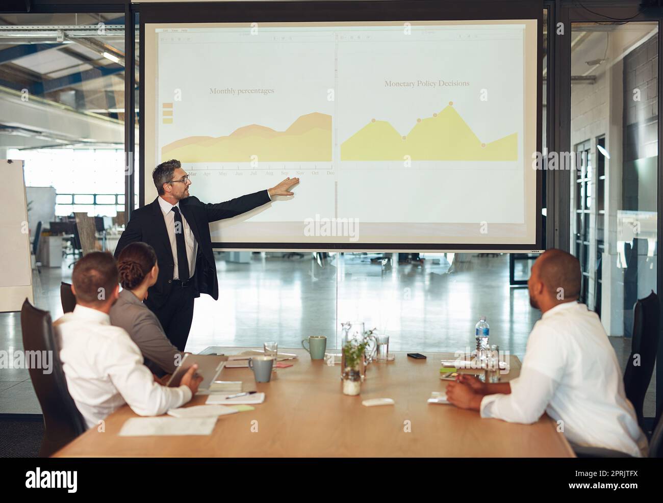 Explaining the companys figures in plain English. an executive giving a presentation on a projection screen to a group of colleagues in a boardroom. Stock Photo