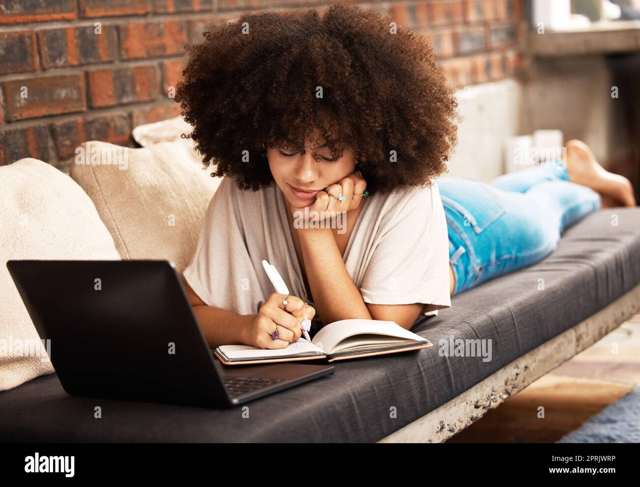 Education, learning and writing with a woman student studying online with her laptop on a sofa in her home living room. Study, growth and development with a female learner taking notes for an exam Stock Photo