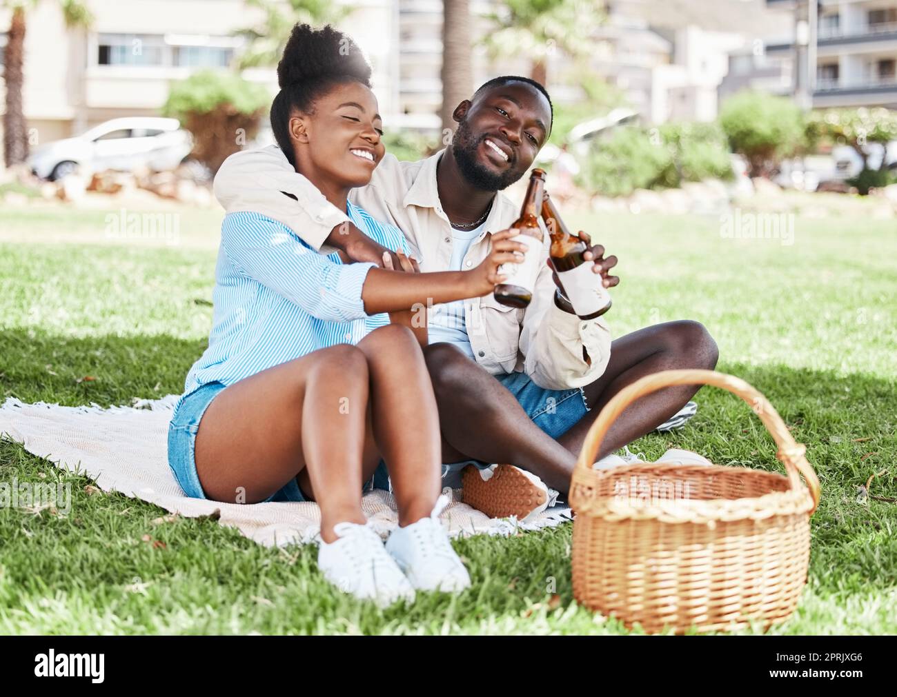 Couple on garden picnic date, black woman and drink bottle of beer together. Young african man, drinking alcohol and happy girl. Outdoor nature, park in city and love relationship time together Stock Photo