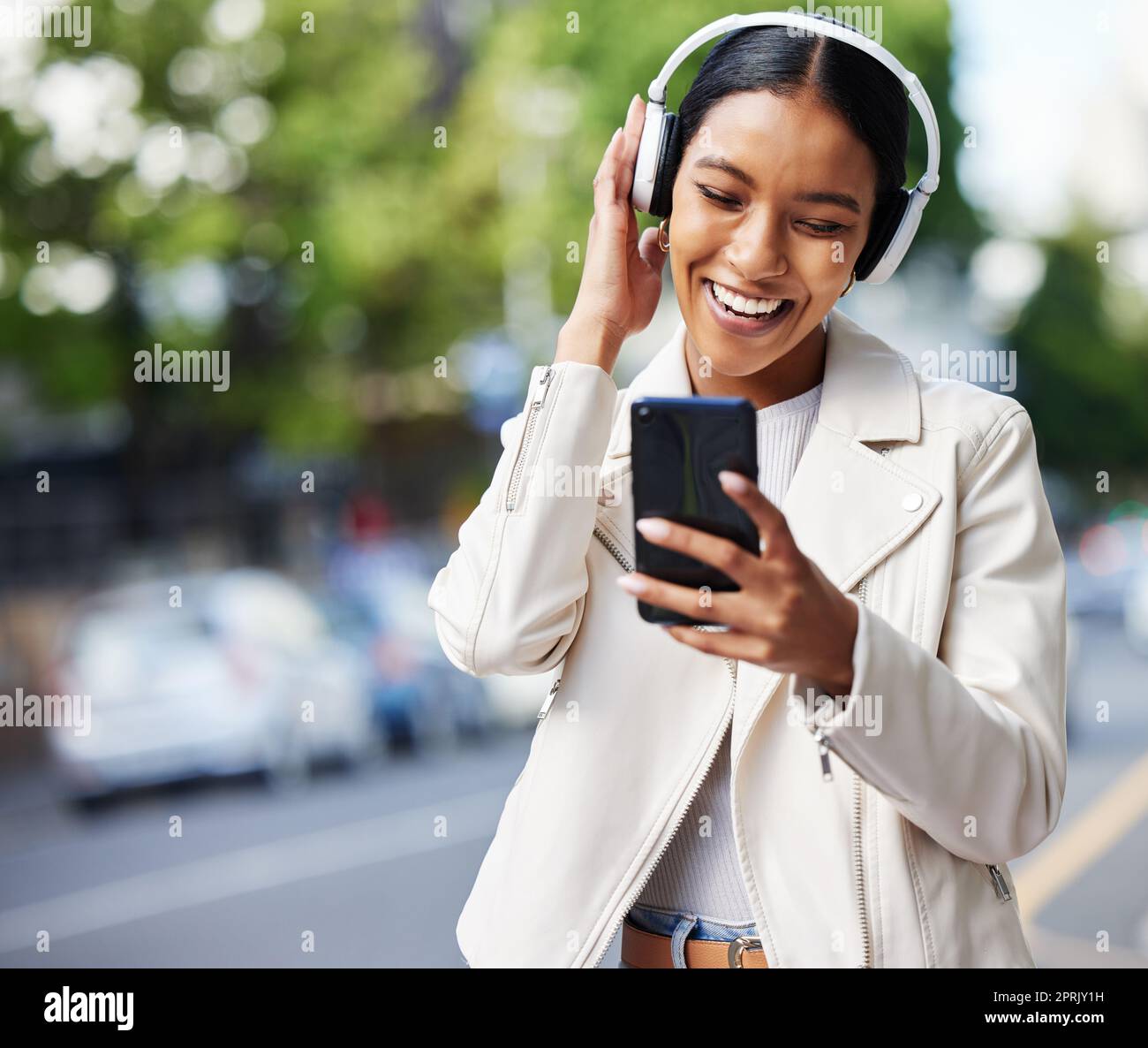 Happy city girl with phone and headphones listening to music, podcast or streaming a online subscription service movie. Black woman watching funny web comedy, internet meme or social media app video Stock Photo