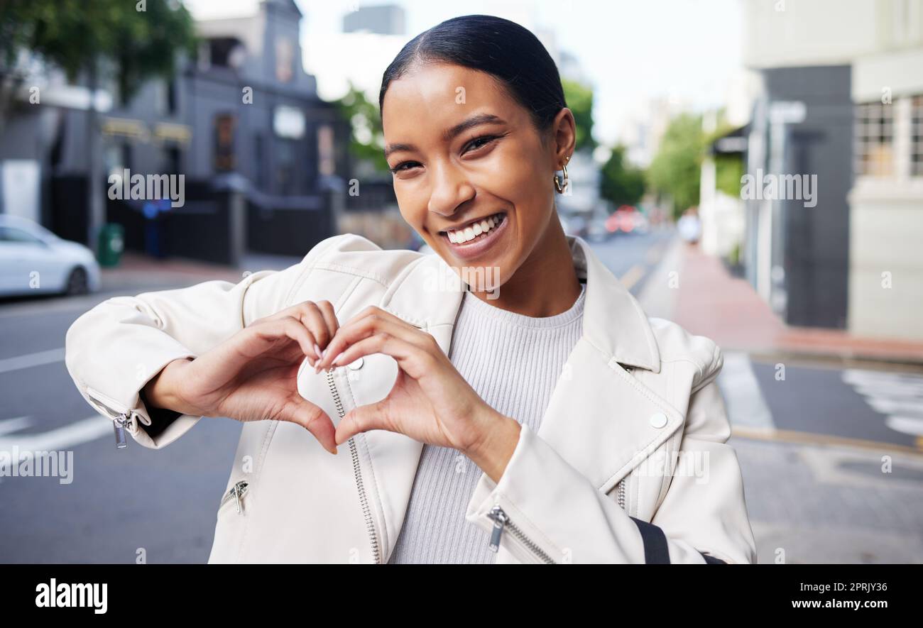 Portrait of a happy woman doing a heart sign with her hands while on health walk in the city street. Beautiful girl with a smile showing the love shape while standing outdoor in the town road. Stock Photo