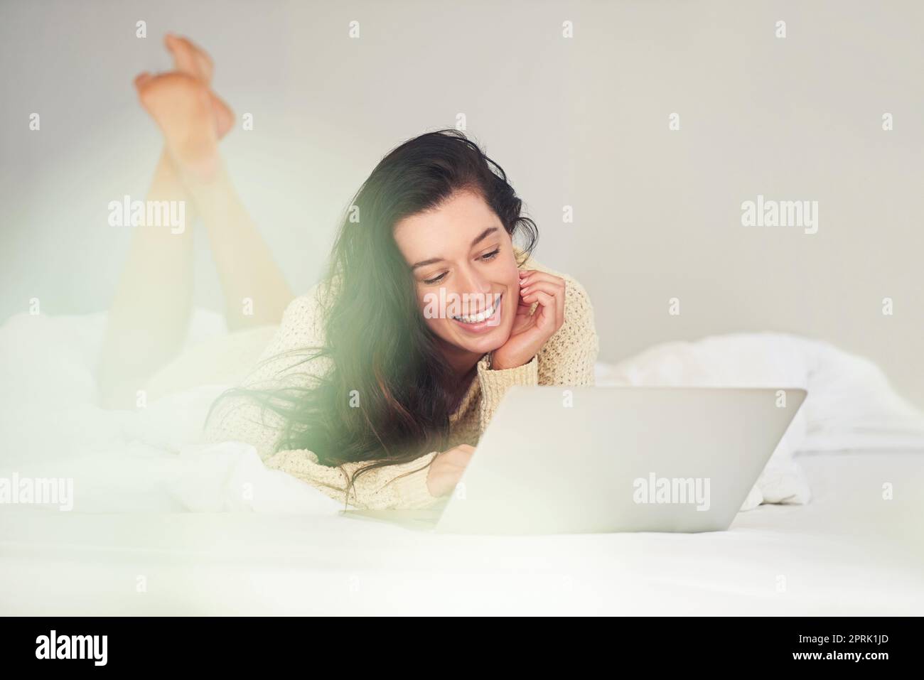 She loves blogging. a young woman using her laptop while lying on her bed. Stock Photo