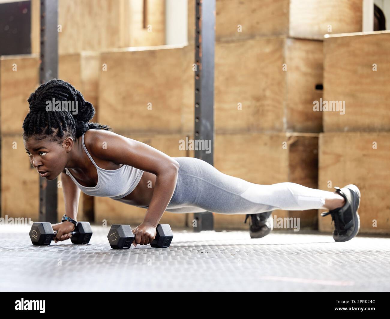 Fitness, training and gym exercise of a sports black woman from Kenya with motivation and focus. African female sport workout with weights in a plank pose doing cardio in a wellness, health studio Stock Photo