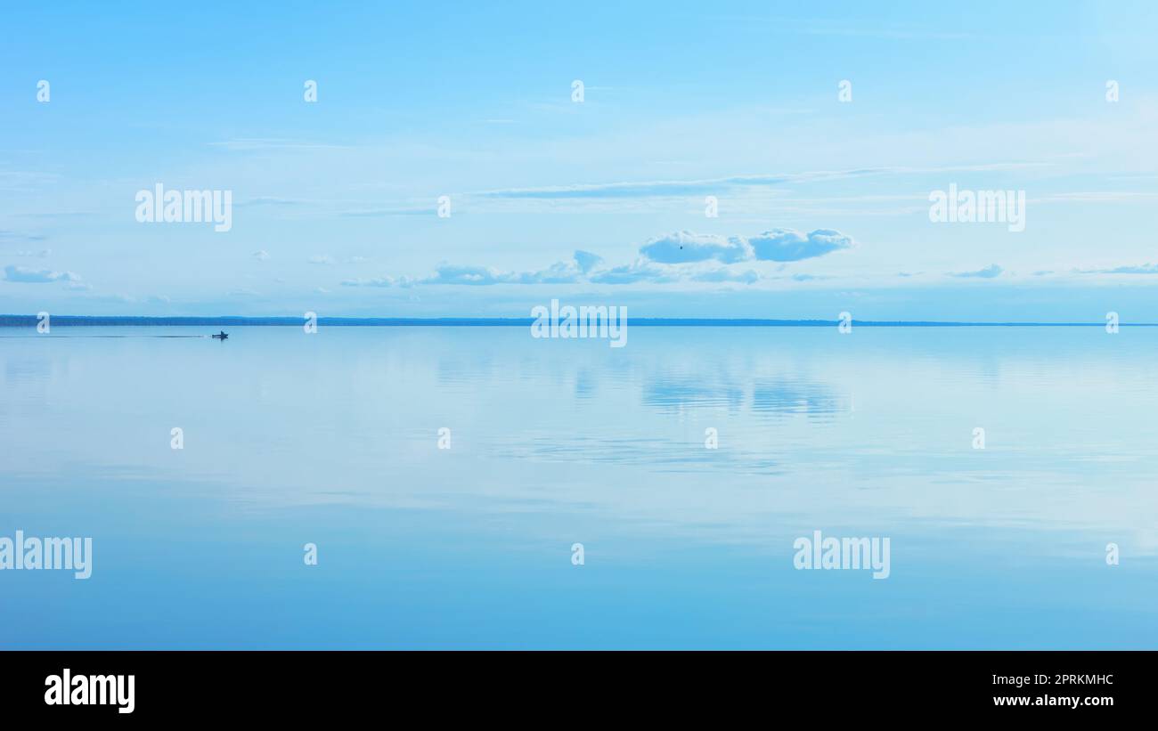 Light blue sky reflected in a calm smooth lake surface. Atmosphere of serenity and tranquility. Summer seascape background with space for copy. Russia Stock Photo