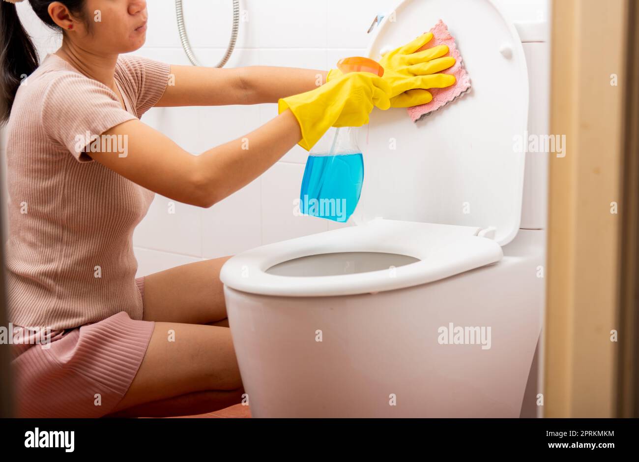 Woman cleaning toilet seat using liquid spray and pink cloth wipe restroom at house, female wearing yellow rubber gloves she sitting and wash cleaner Stock Photo
