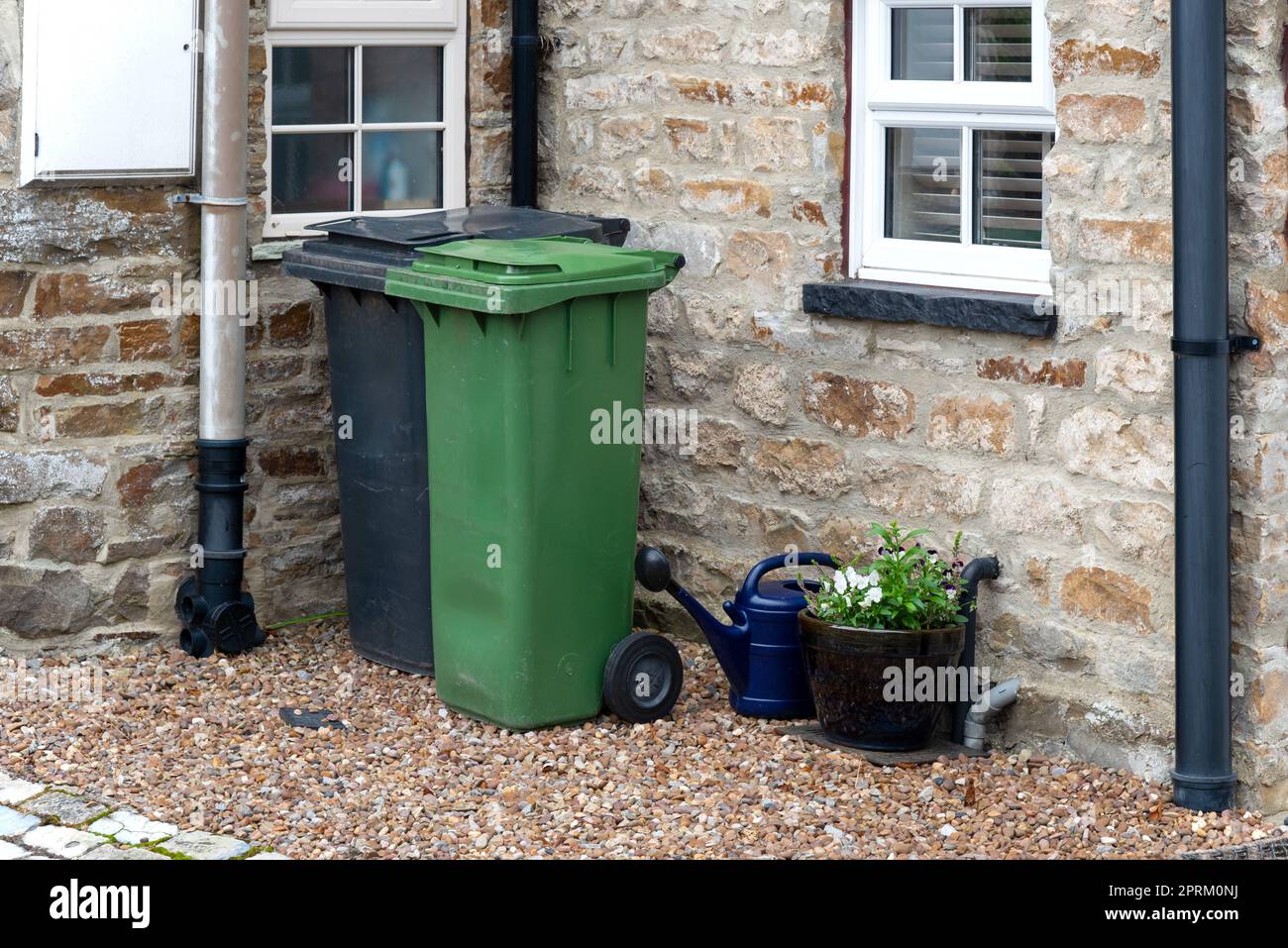 A Green and a black wheelie bin in front of a house entrance somewhere in a small village near