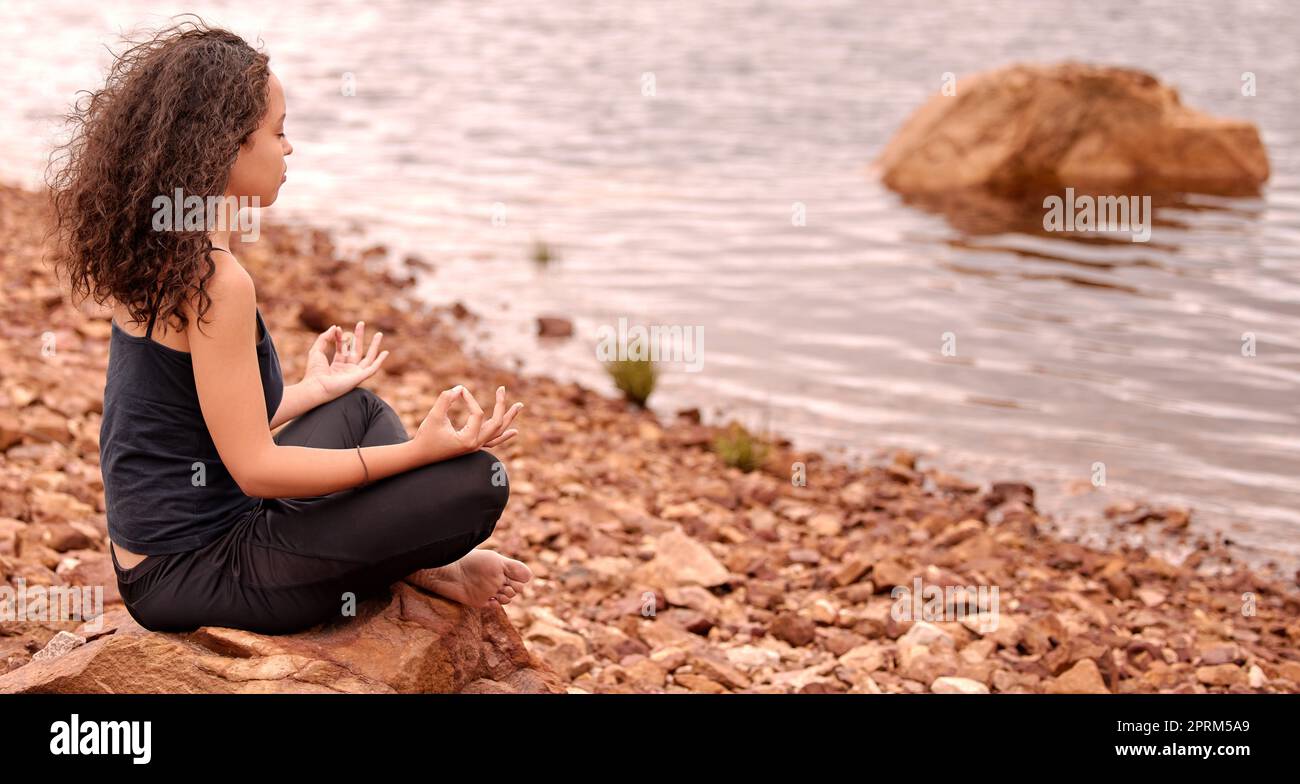 This is where I come to meditate. a young woman medicating while sitting by a lake Stock Photo