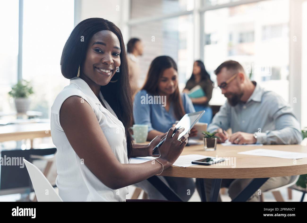 Im on the correct career path. Cropped portrait of an attractive young businesswoman sitting and using a tablet while her coworkers work behind her Stock Photo