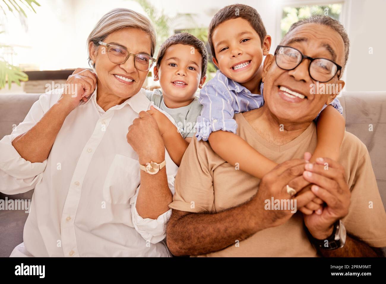 Love, happy family and kids relax with grandparents on a sofa, hug and bonding in a living room. Portrait, seniors and children embracing, laughing an Stock Photo