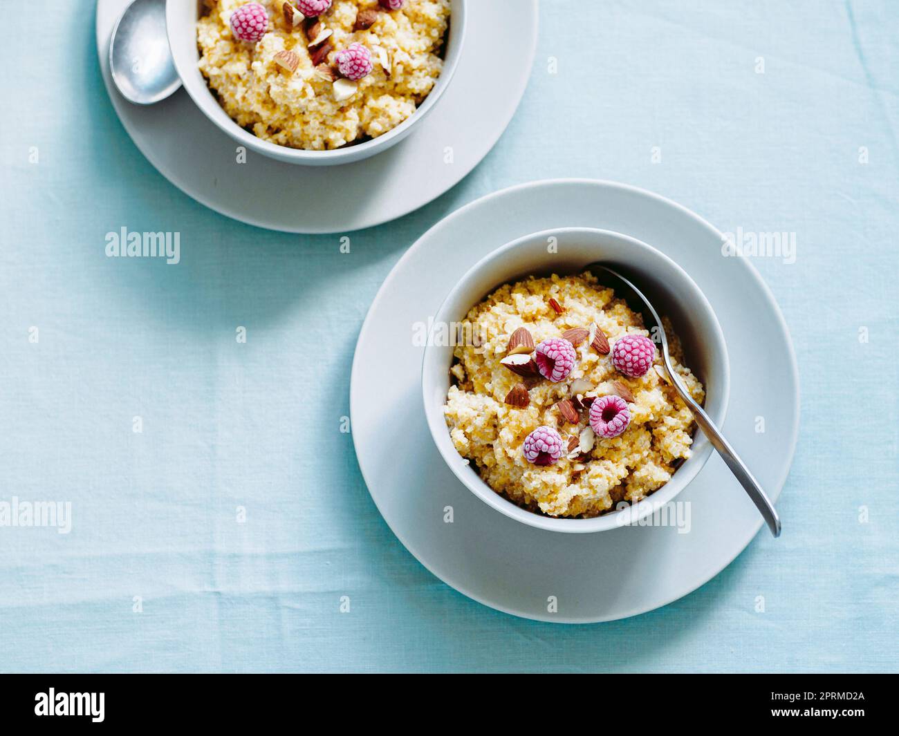 Quinoa porrige on tabletop. Two bowl wit quinoa milk porridge with berries and almond. Frozen raspberries in quinoa porrige Stock Photo