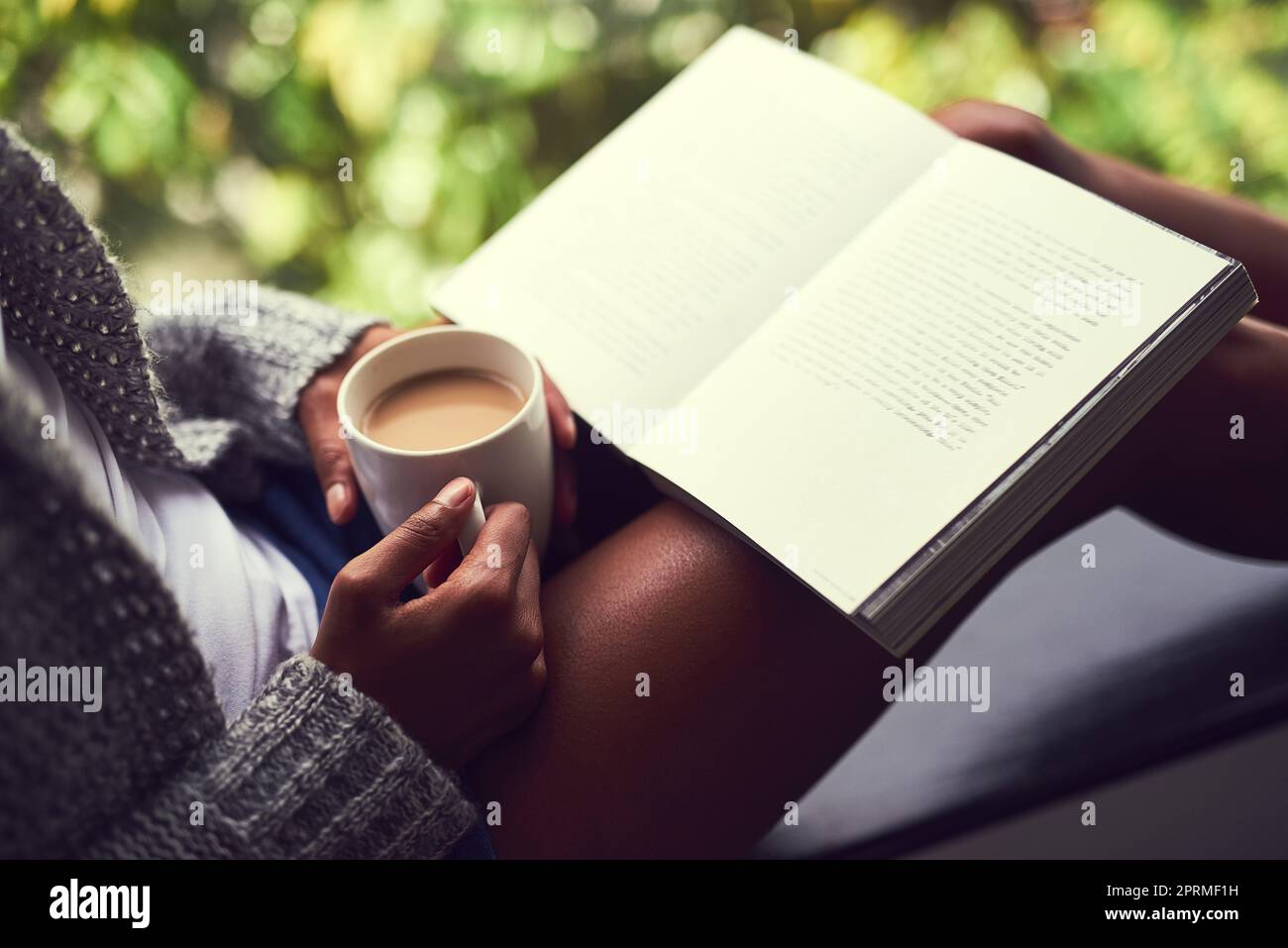 Getting stuck in her favourite book. an unidentifiable young woman reading a book while enjoying a cup of coffee at home. Stock Photo