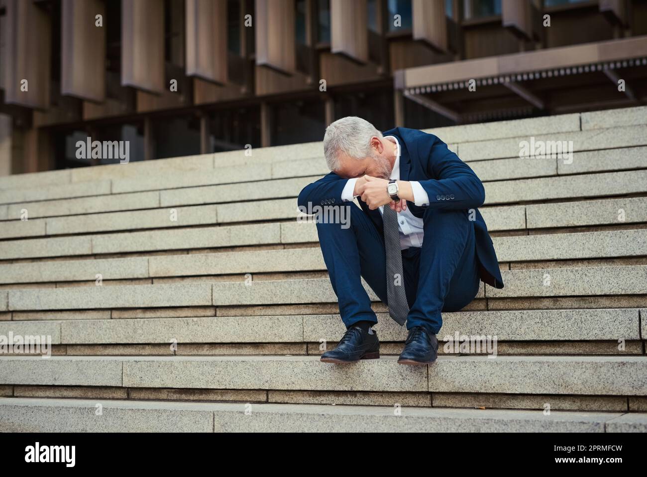 Not his best day. a dejected businessman sitting on the stairs outside his office with his head in his hands. Stock Photo