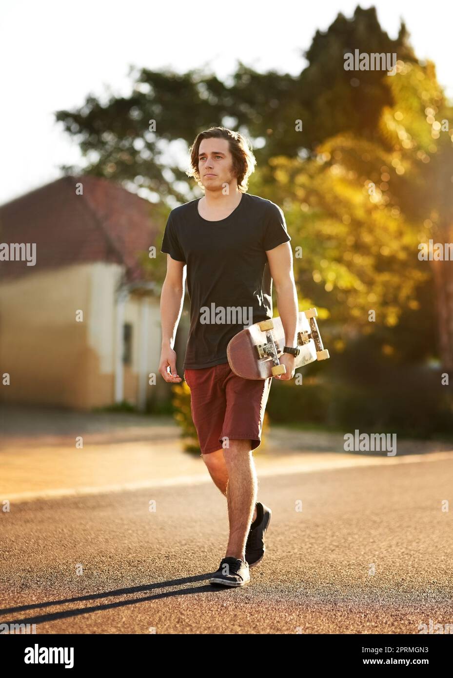 Heading off to the skatepark. a young man walking with is skateboard in hand outside. Stock Photo