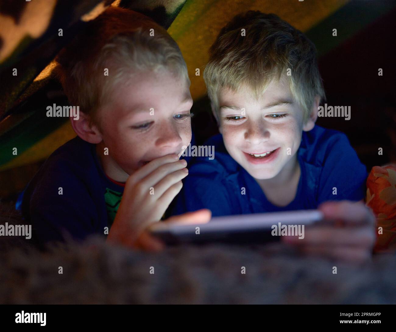 I wont tell on you if you let me play. siblings using a digital tablet under their fort at home. Stock Photo