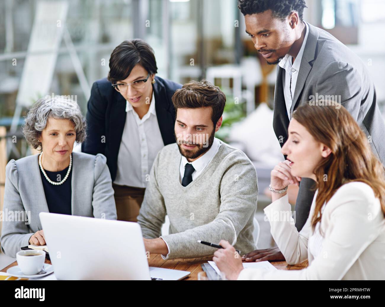 Tackling their challenges with the help of technology. a group of businesspeople working together on a laptop in an office. Stock Photo