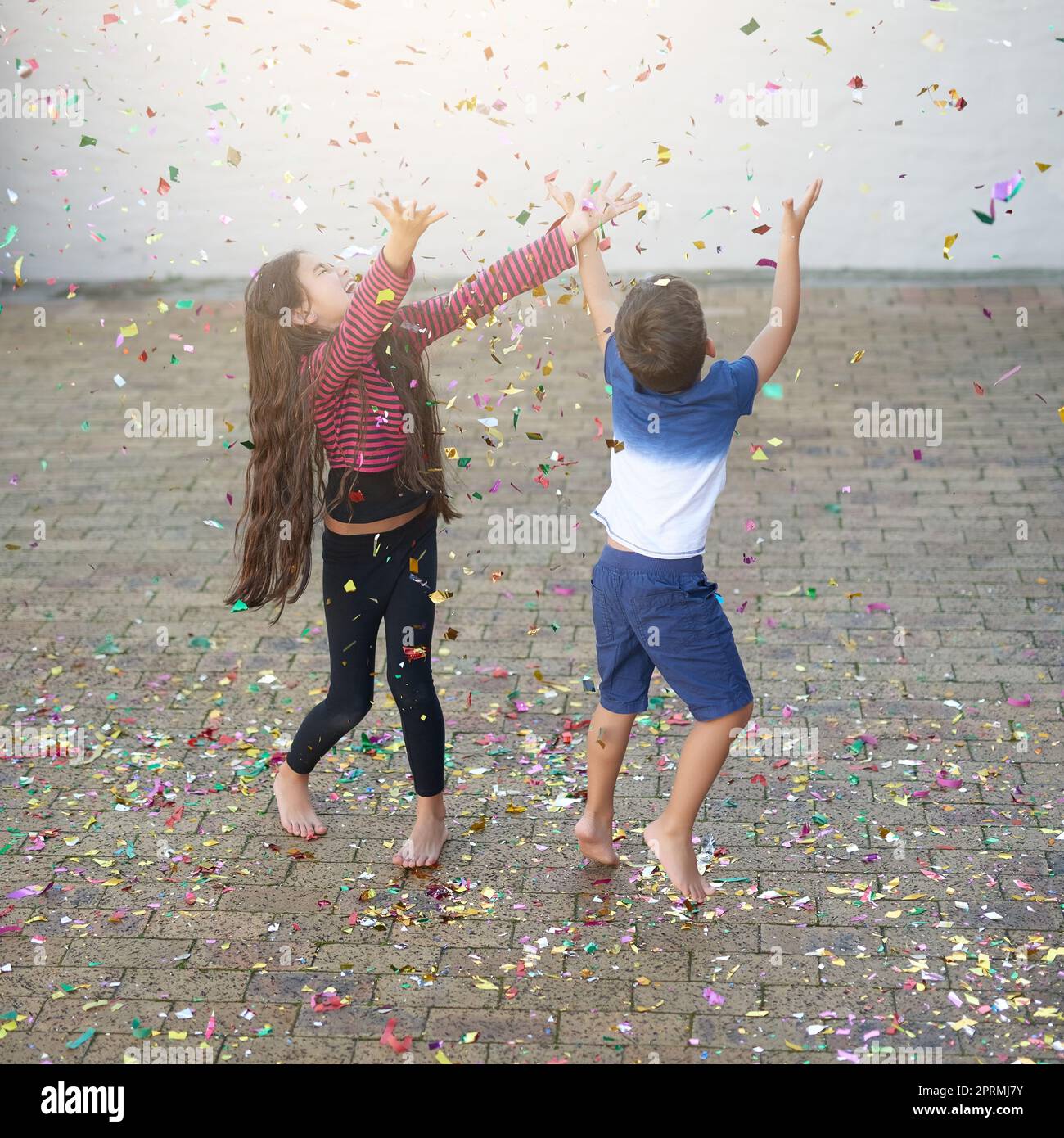 Confetti turns any situation into a celebration. a cute little boy and girl jumping to catch confetti as it falls outside their house. Stock Photo