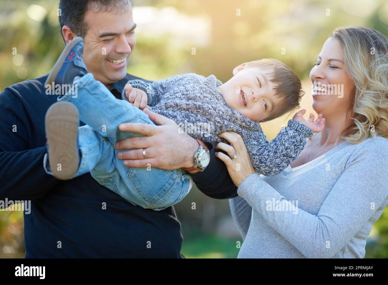 His laugh is just the cutest. parents bonding with their little boy outside. Stock Photo