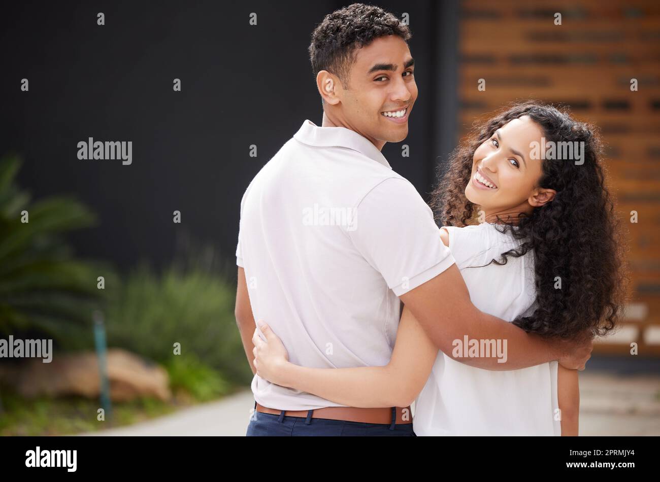 Portrait, love and couple happy in front of new home or house hug as they stand on driveway with a smile. Real estate, investment in future and property with man and woman spending time together. Stock Photo