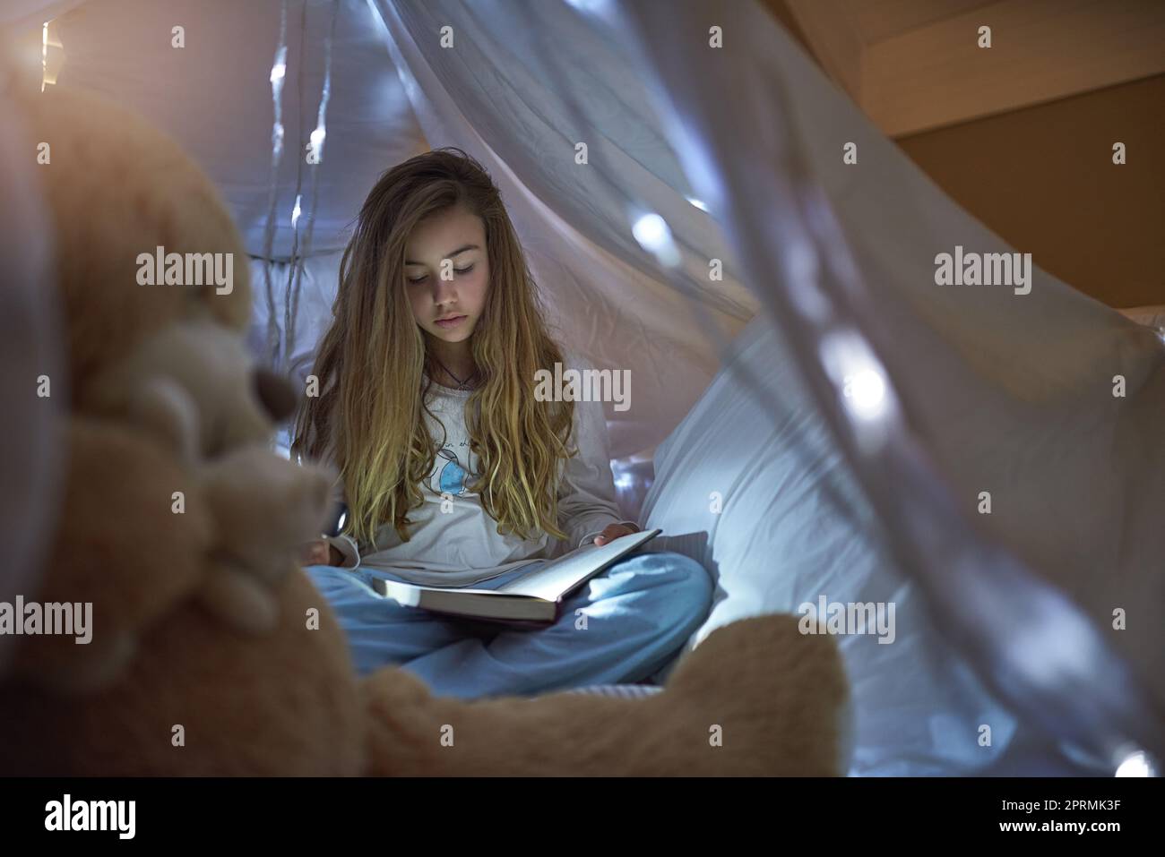 Nothing like a good book before bedtime. a young girl reading a book under a blanket fort at