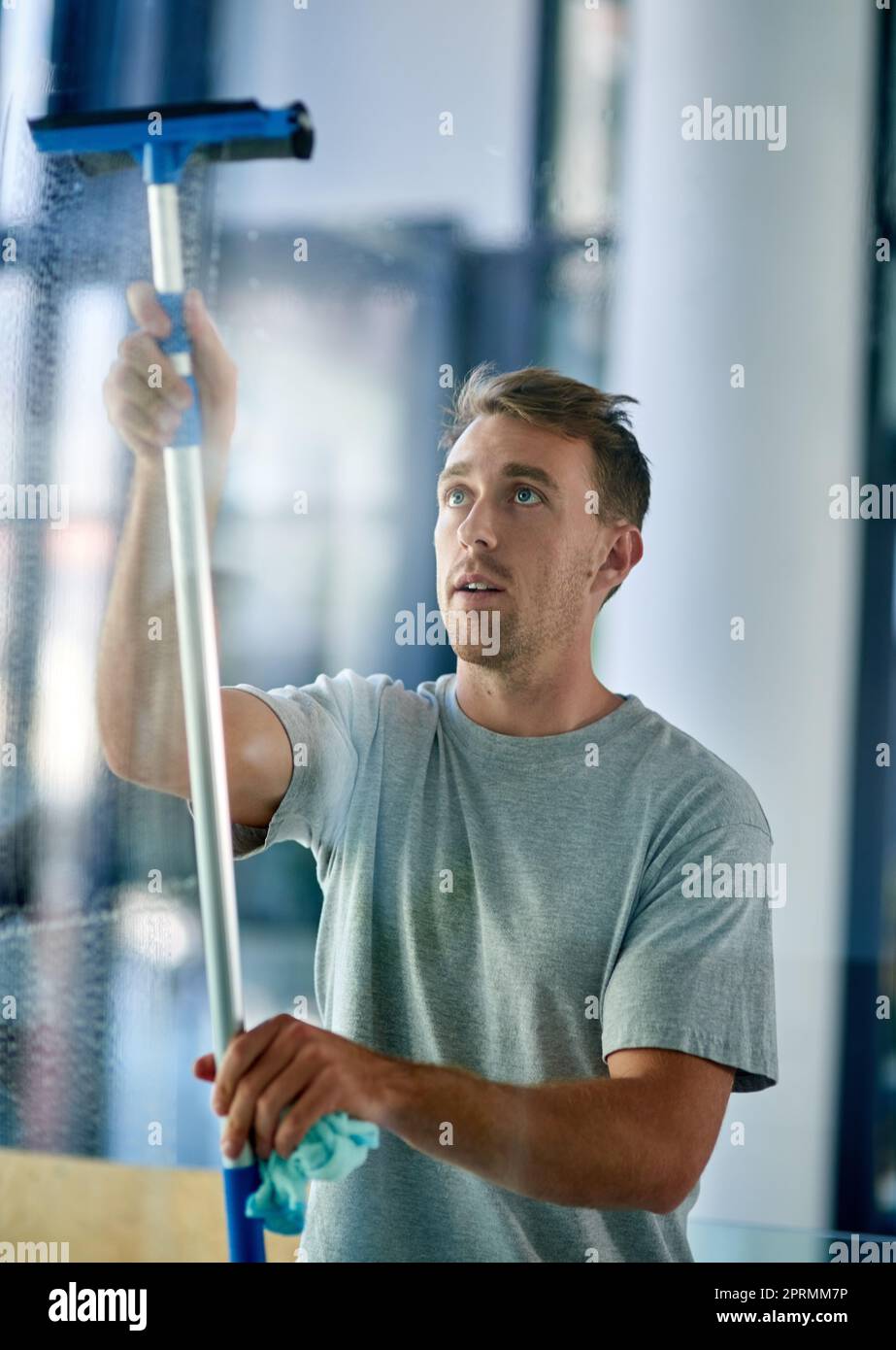 Squeaky clean. a young man cleaning the windows in the office Stock