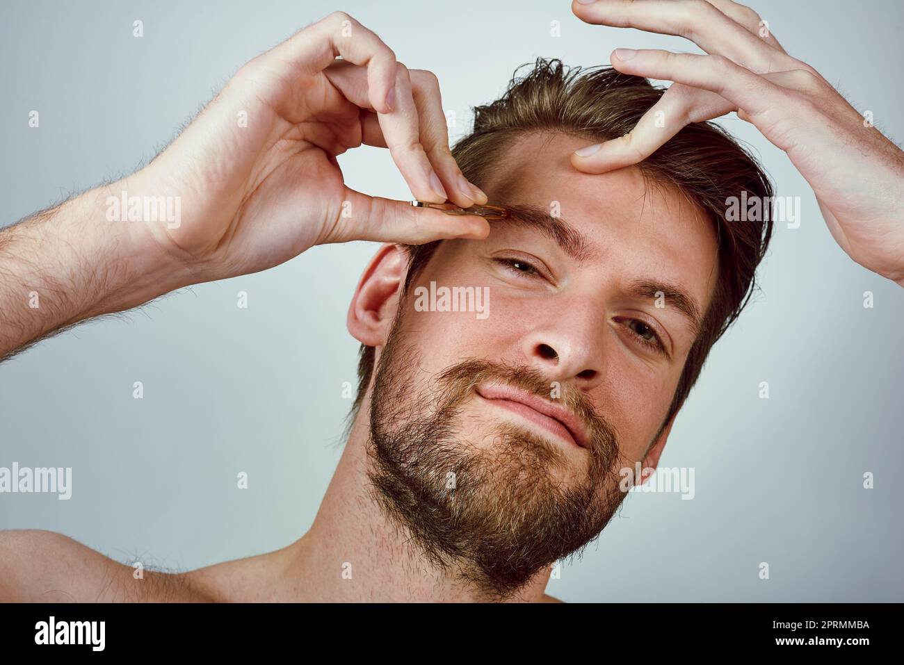 Be the boss of your brows. Studio shot of a handsome young man plucking his eyebrows against a gray background. Stock Photo