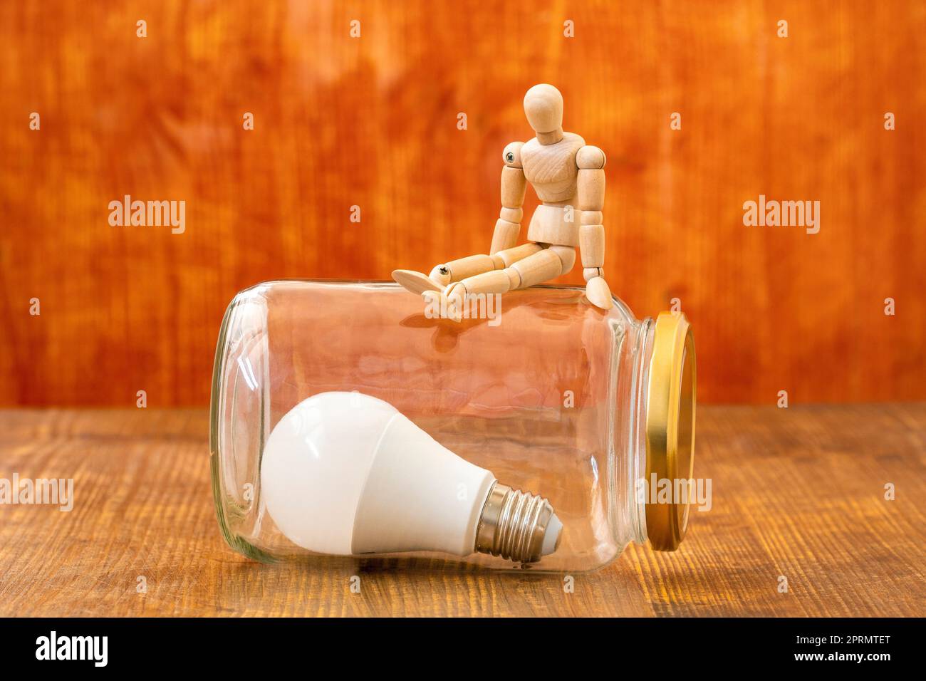 Wooden mannequin sitting on the glass jar with a lightbulb inside Stock Photo