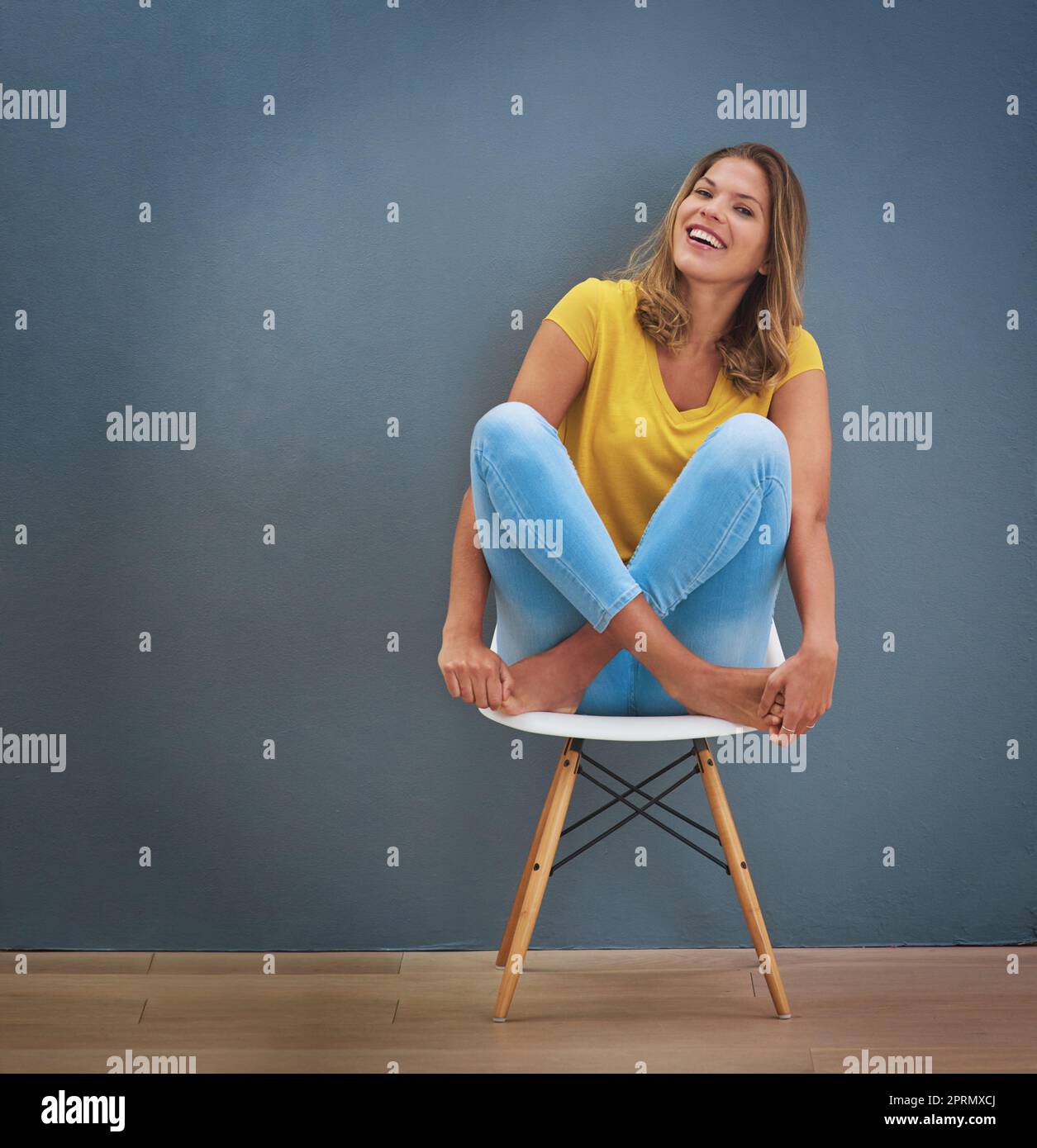 Be happy and smile. a young woman sitting on a chair against a gray ...