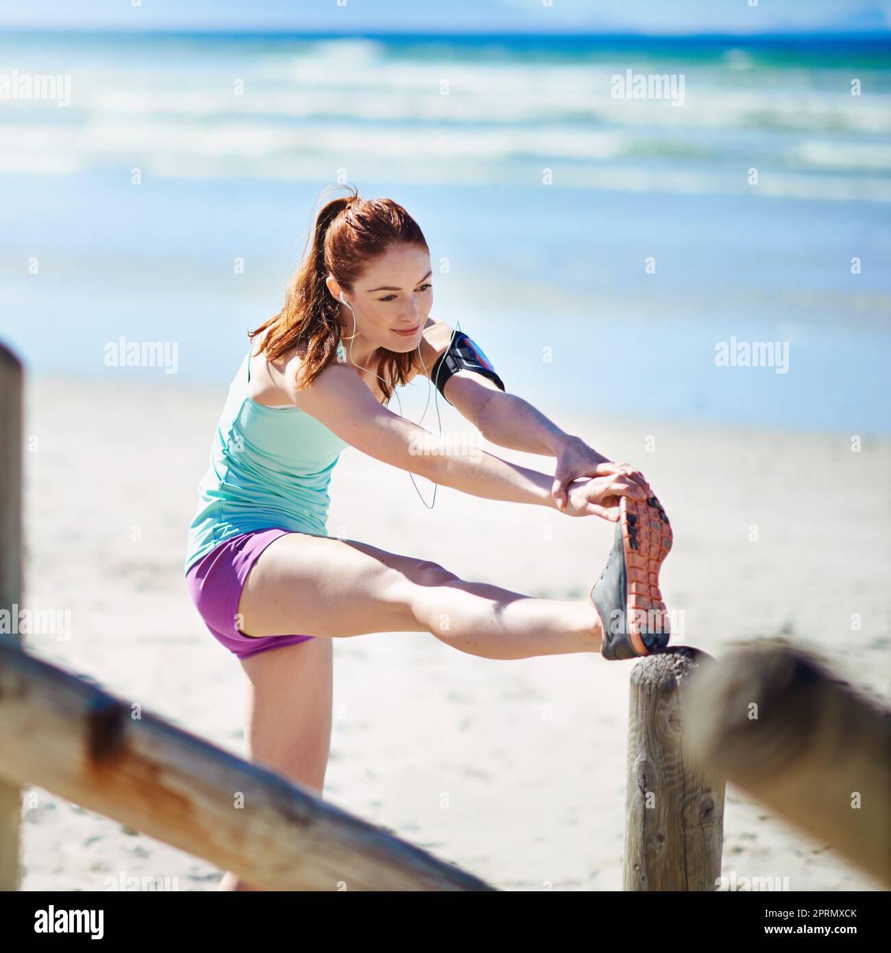 Dont forget to warm up. a young woman stretching before a work out on the beach. Stock Photo