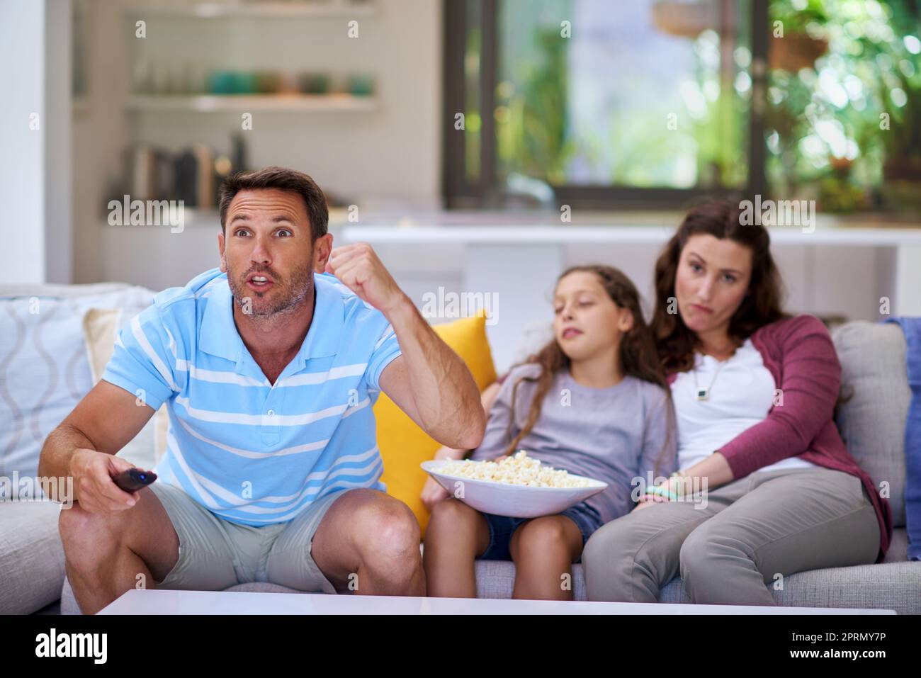 Cheering his team on. a man watching sports on the TV while is family sits bored in the background. Stock Photo