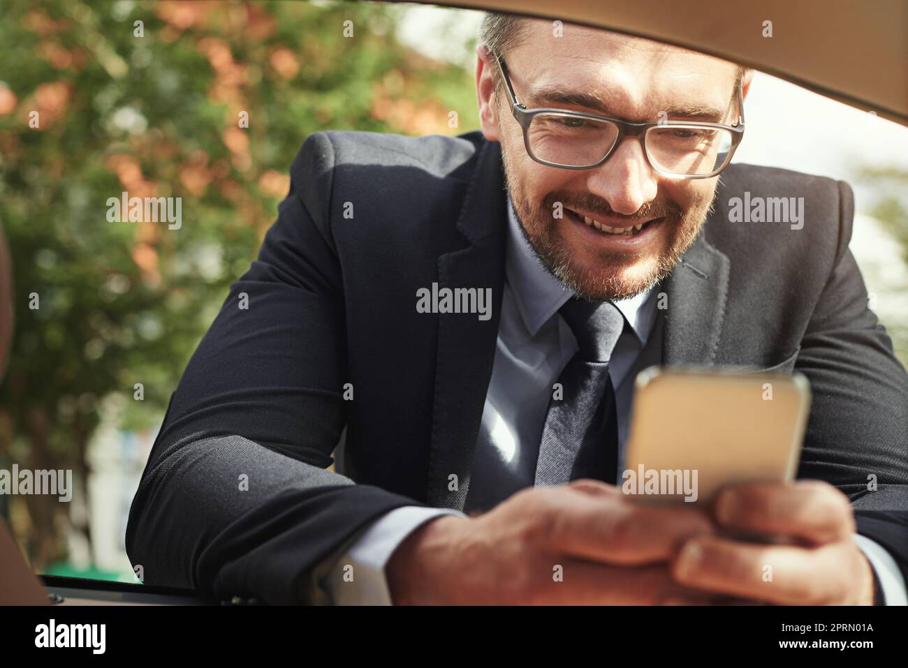 Stopping to send a text. a businessman using a phone while leaning against his car. Stock Photo