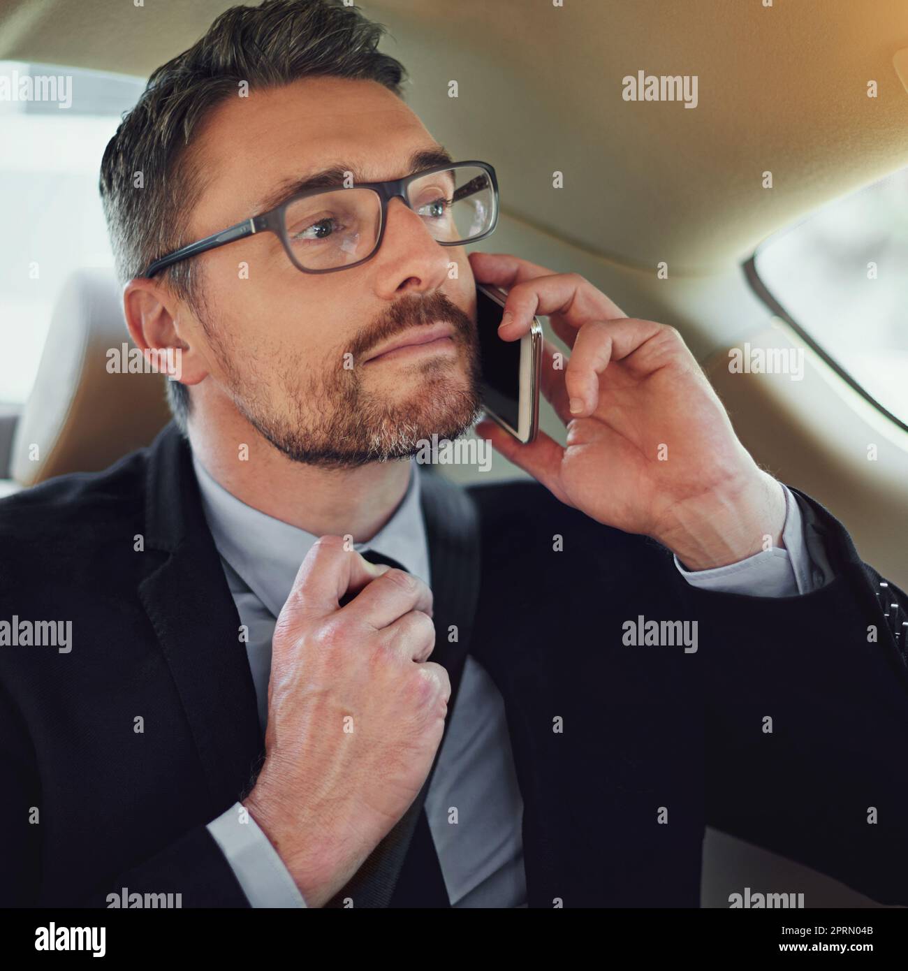 Ill be there in 5 minutes. a businessman using his cellphone while sitting in the backseat of a car. Stock Photo