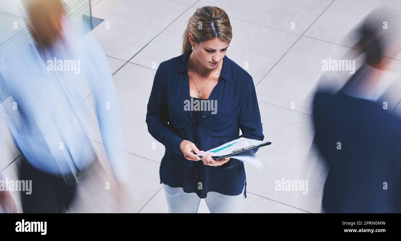 Business employee reading paperwork, crowd of people walking fast and serious corporate white woman stopping in lobby hall. Busy office building, hold company documents and people traffic blur motion Stock Photo
