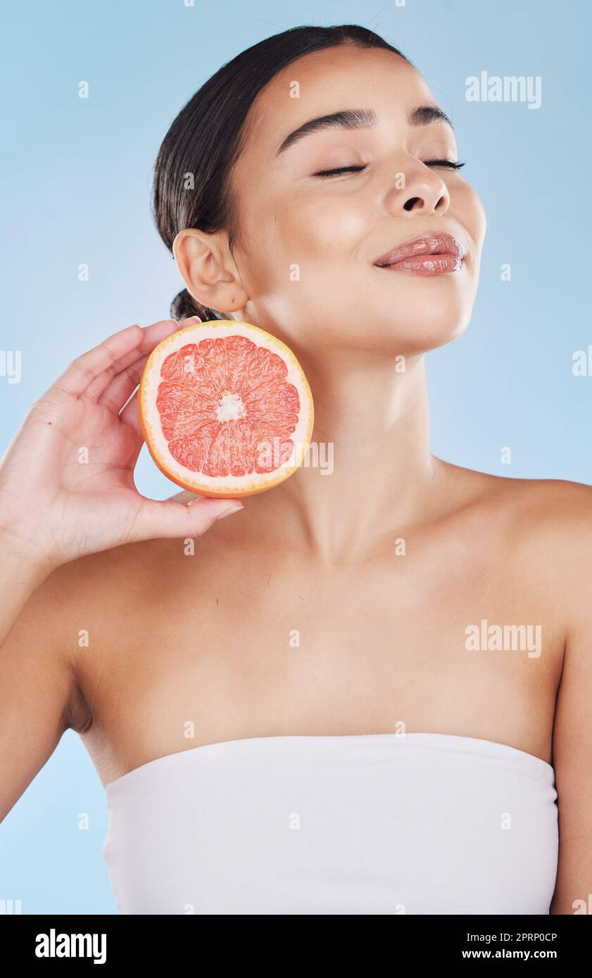 Grapefruit, woman skincare and wellness fruit for face grooming, wellness and diet health on a blue background in studio. Happy, smile and beauty brazilian model with vitamin c food product in hands Stock Photo