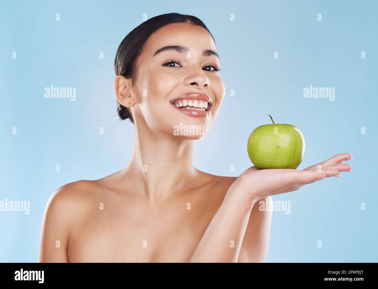 Health, food and apple diet with happy woman holding fruit against blue background. Portrait of a young female excited by weight loss and nutrition, showing benefits of healthy, balance lifestyle Stock Photo