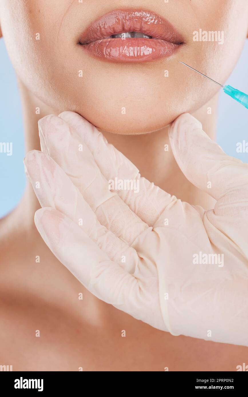 Botox, surgery and lips with a woman getting an injection in her mouth for beauty, skincare and medicine in studio on a blue background. Filler, product and cosmetics with a young female model inside Stock Photo