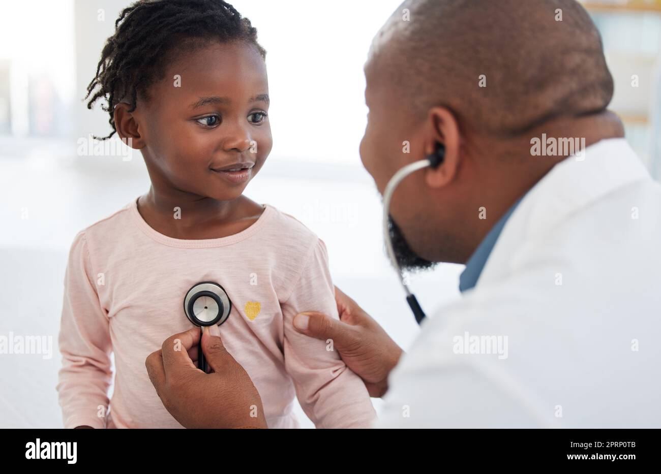 Healthcare, pediatrician and child heart doctor with a patient at hospital, exam on chest with a stethoscope. Black girl smile at pediatric surgeon, talking to a friendly, caring physician she trust Stock Photo