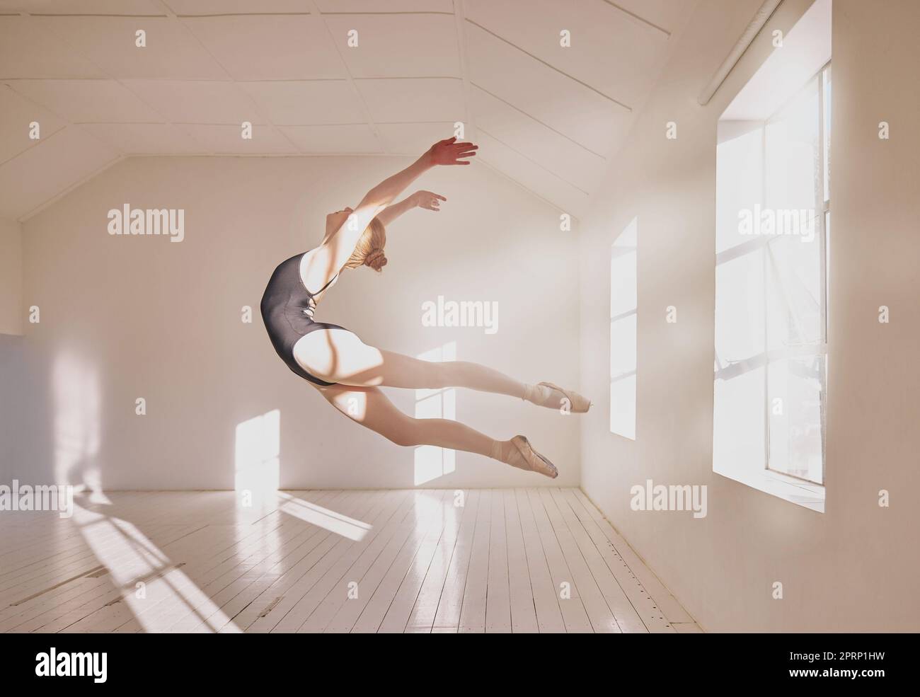 Woman ballet dancer dancing in a dance studio mockup white walls and sunlight. Young professional girl, art or sports student jumping mid air technique in a creative ballerina class Stock Photo