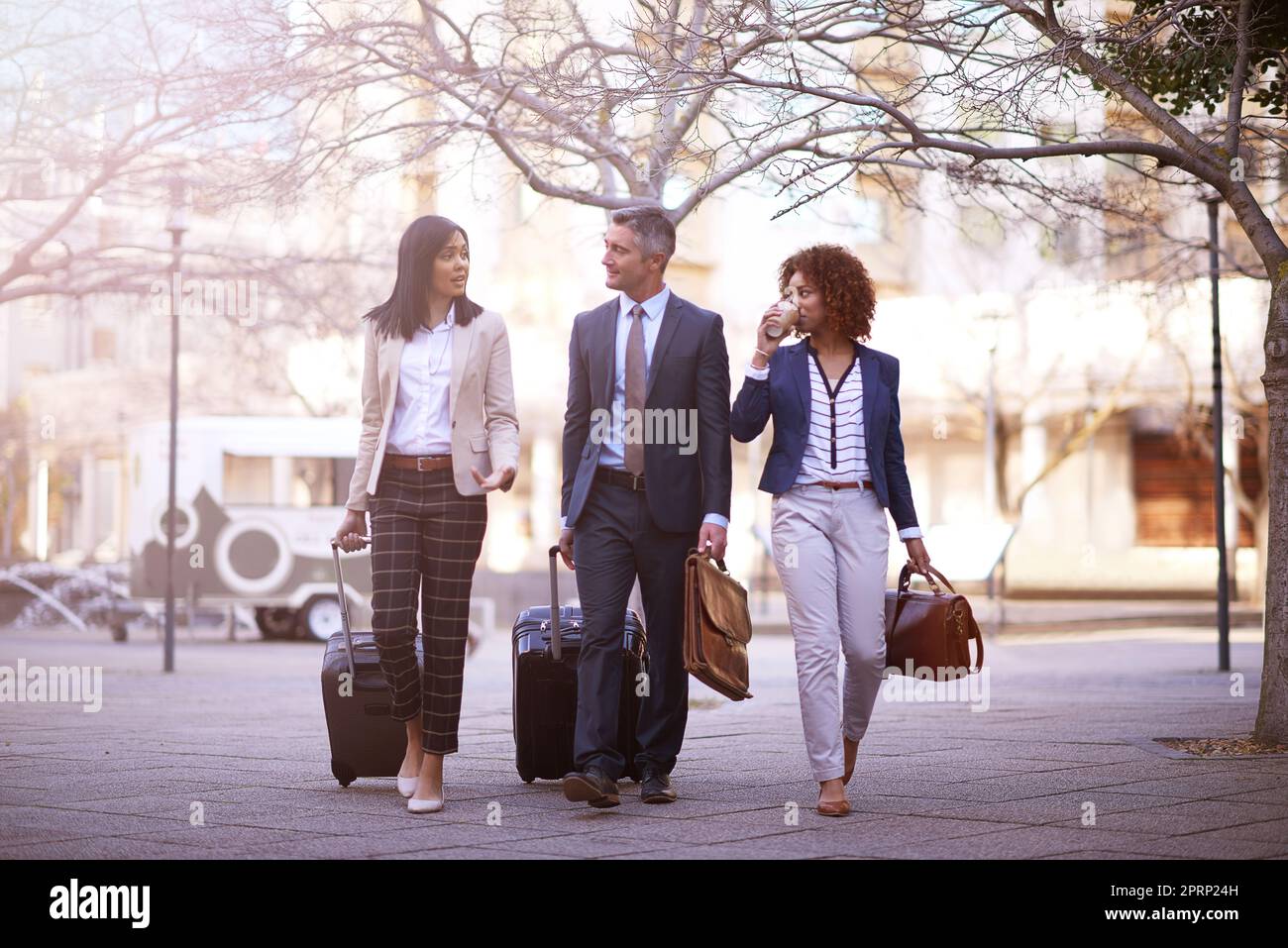 Business on the move. a group of business people walking and talking to each other while carrying their luggage outside. Stock Photo