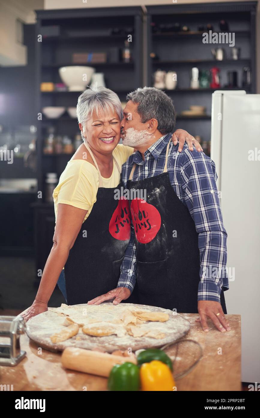 Whipping up something delicious. a happy mature couple sharing a tender moment with a kiss while cooking together at home. Stock Photo