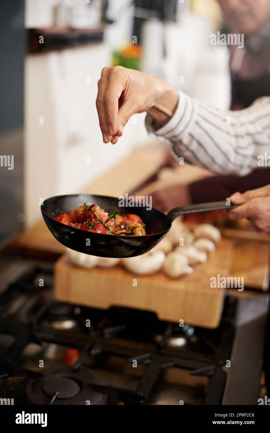 The missing ingredient. a unrecognizable persons hand adding salt to a pan of tomatoes in the kitchen. Stock Photo