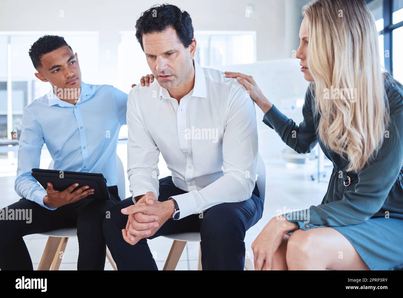 Business, support group and man at the office in depression with supportive colleagues at the workplace. Male employee with mental health problems in divorce, grief or loss with helpful coworkers. Stock Photo