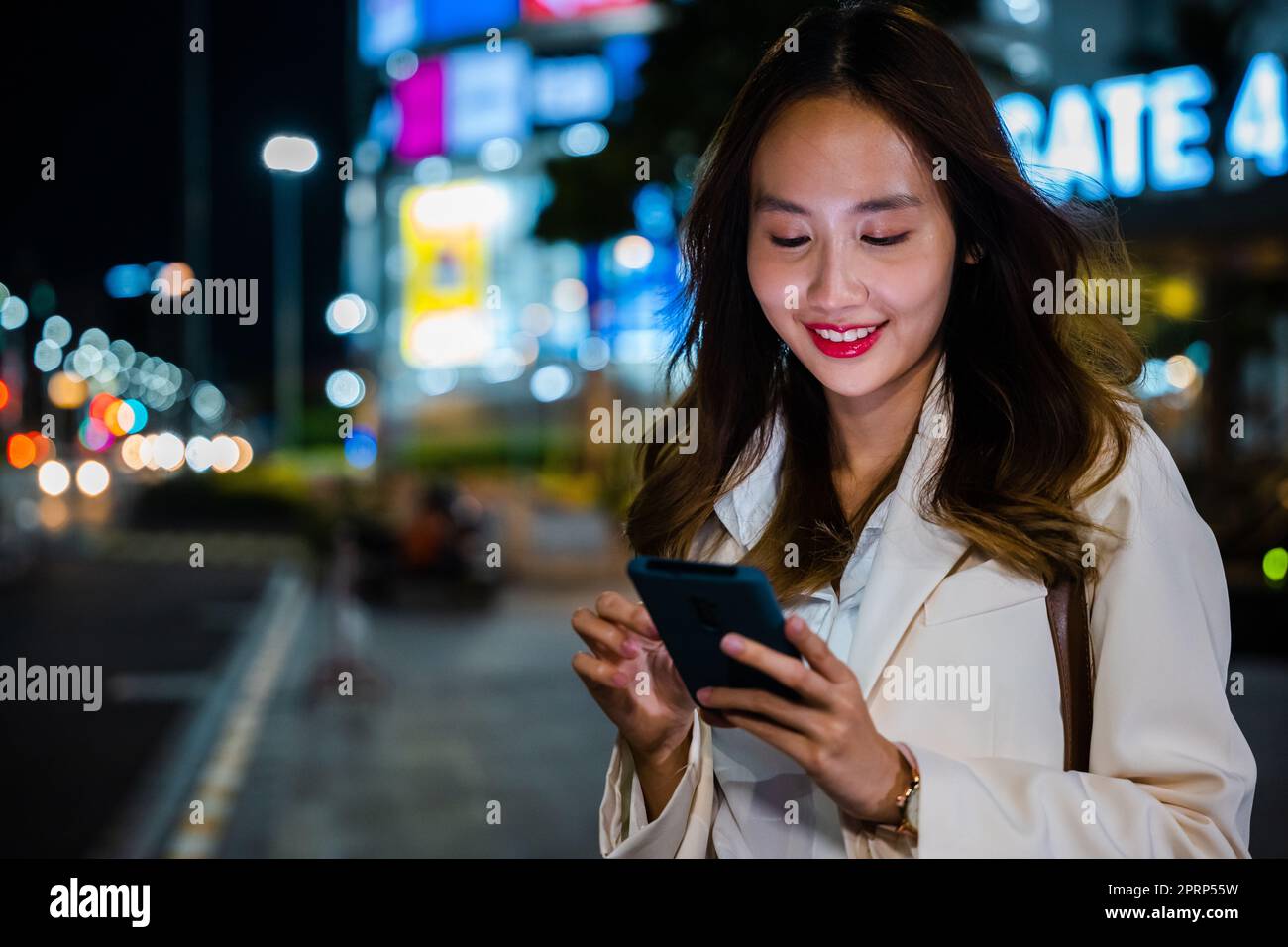 Business woman using mobile phone walking through night city street Stock Photo