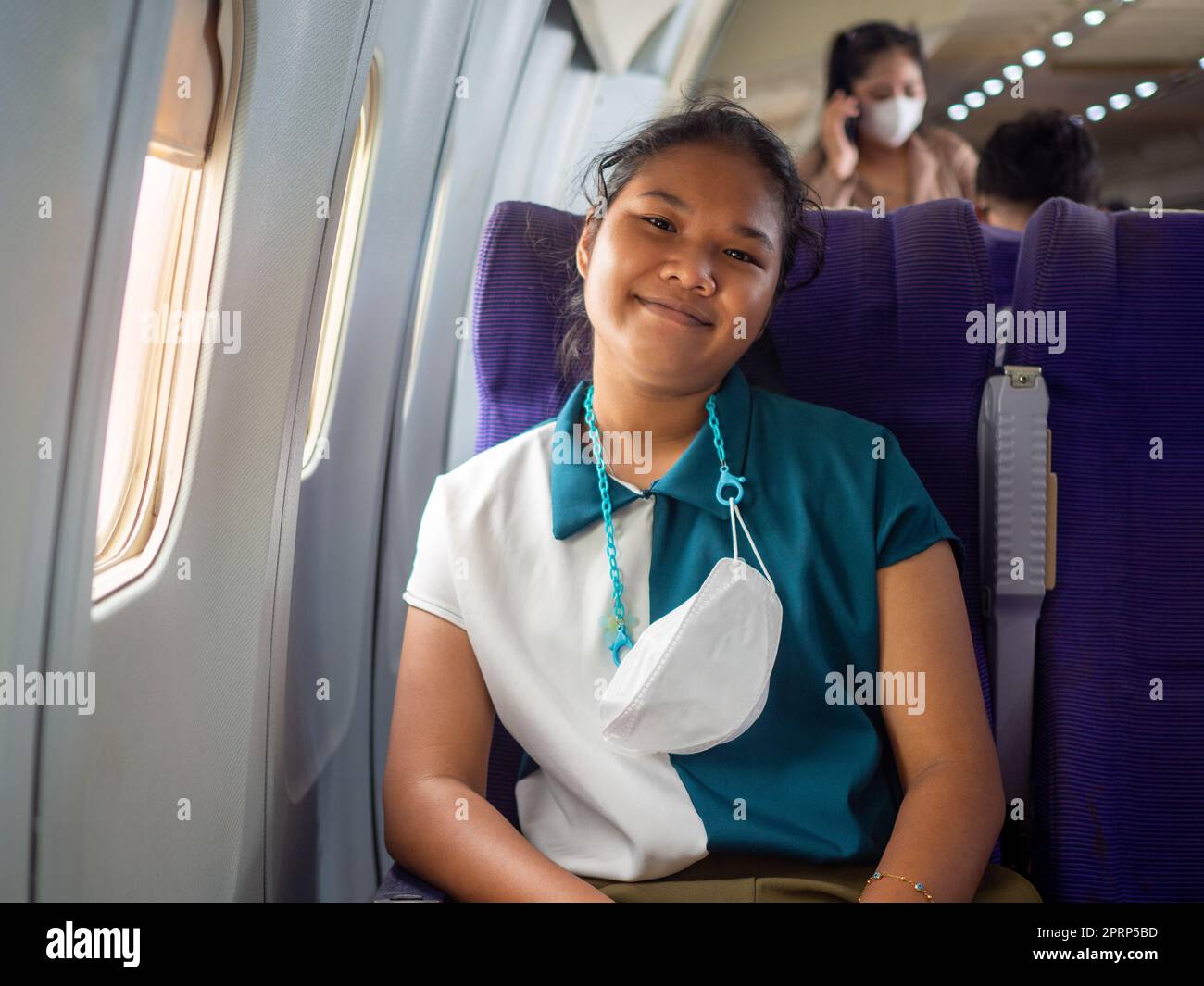 A woman wearing a mask is sitting by the window of an airplane. Stock Photo
