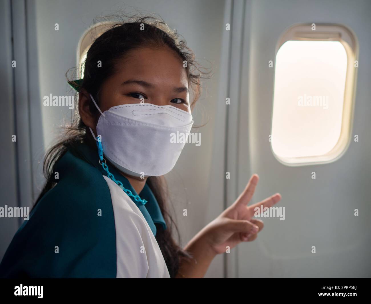 A woman wearing a mask is sitting by the window of an airplane. Stock Photo