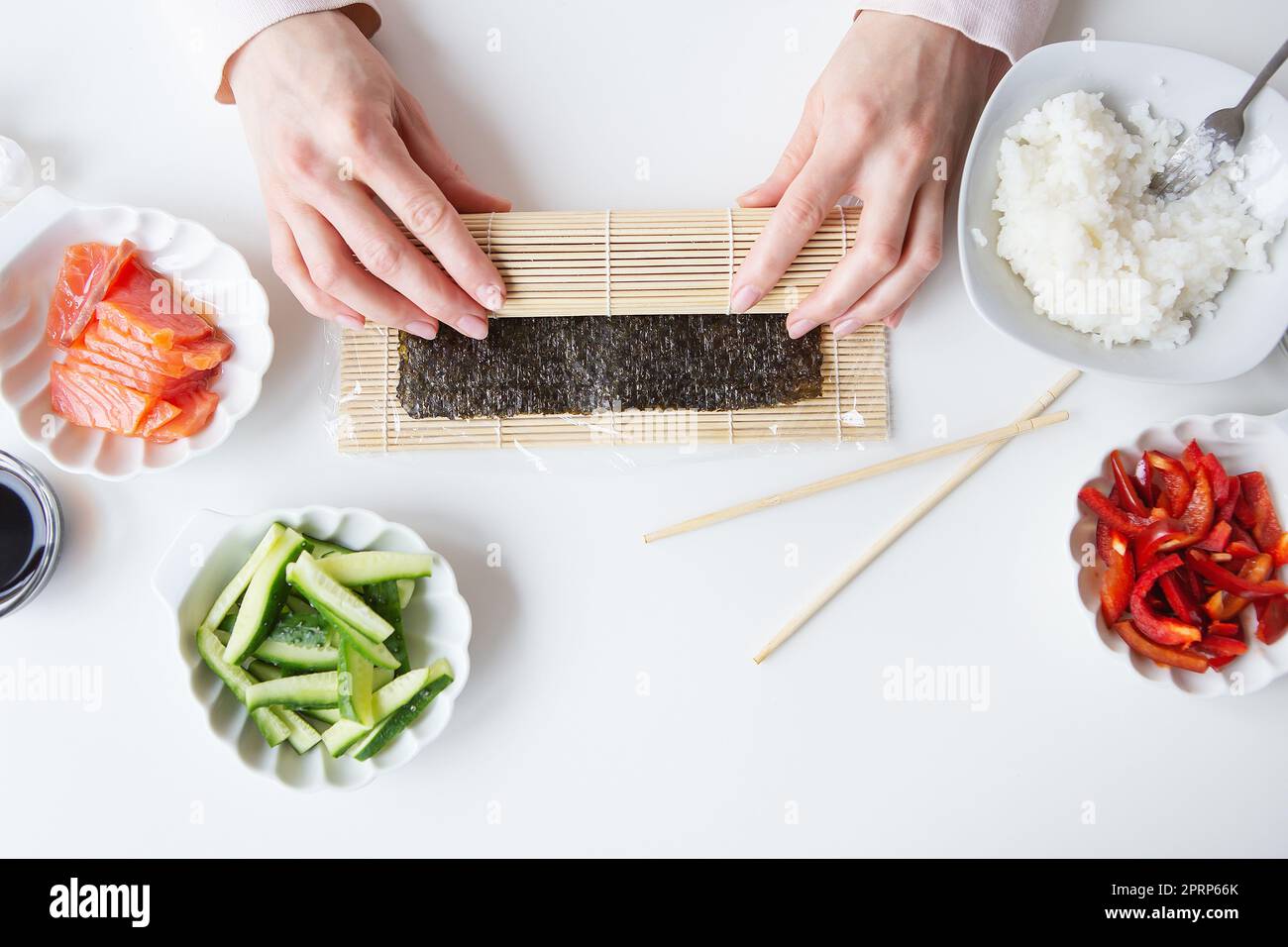 Sushi preparation process, the girl makes sushi with different flavors - fresh salmon, caviar, avocado, cucumber, ginger, rice. Stock Photo