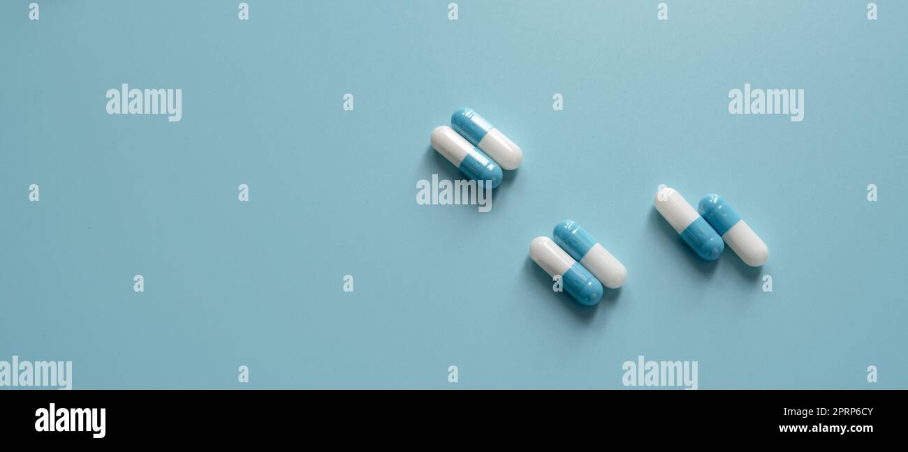 Blue and white capsule pills on blue background. Prescription drugs. Pharmaceutics background. Pharmaceutical industry. Dose of medicine for treating illness. Healthcare and medicine. Medical care. Stock Photo