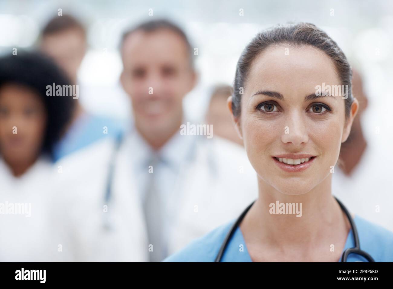 You can trust this team of experts. Happy female doctor smiling at the camera with her colleagues in the background. Stock Photo