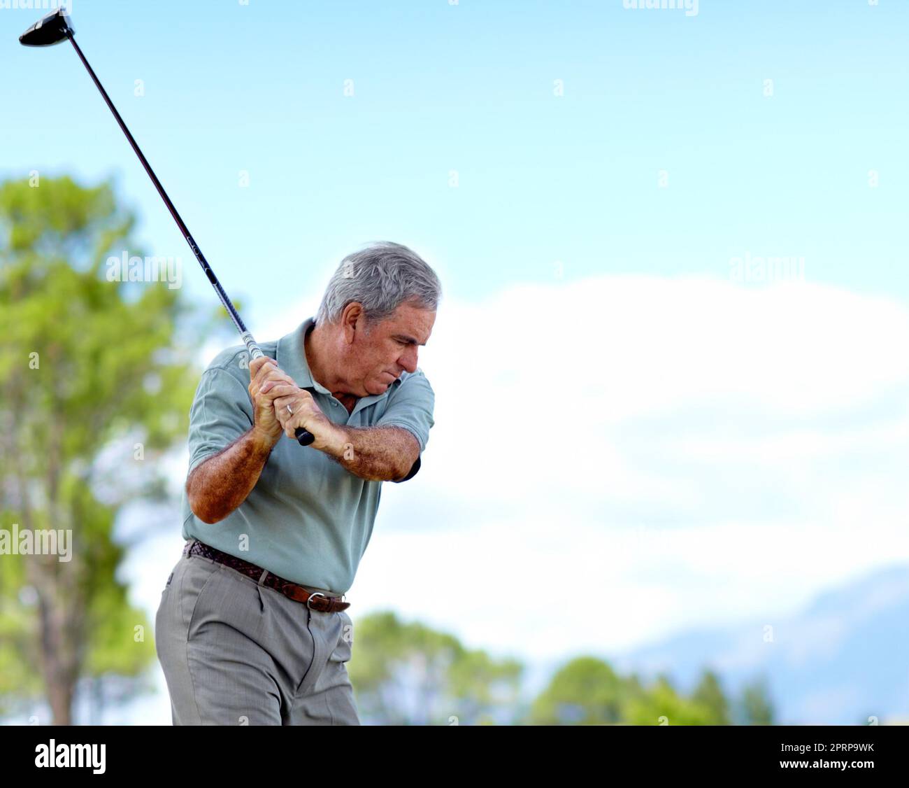 In full swing. Profile of a senior male concetrating as he swings his driver on a golf course Stock Photo
